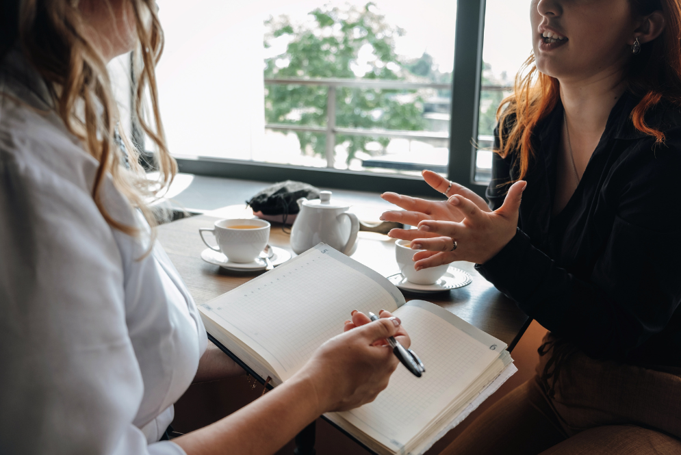 Two women are talking while one of them is holding a pen and a notebook - expand therapy practice