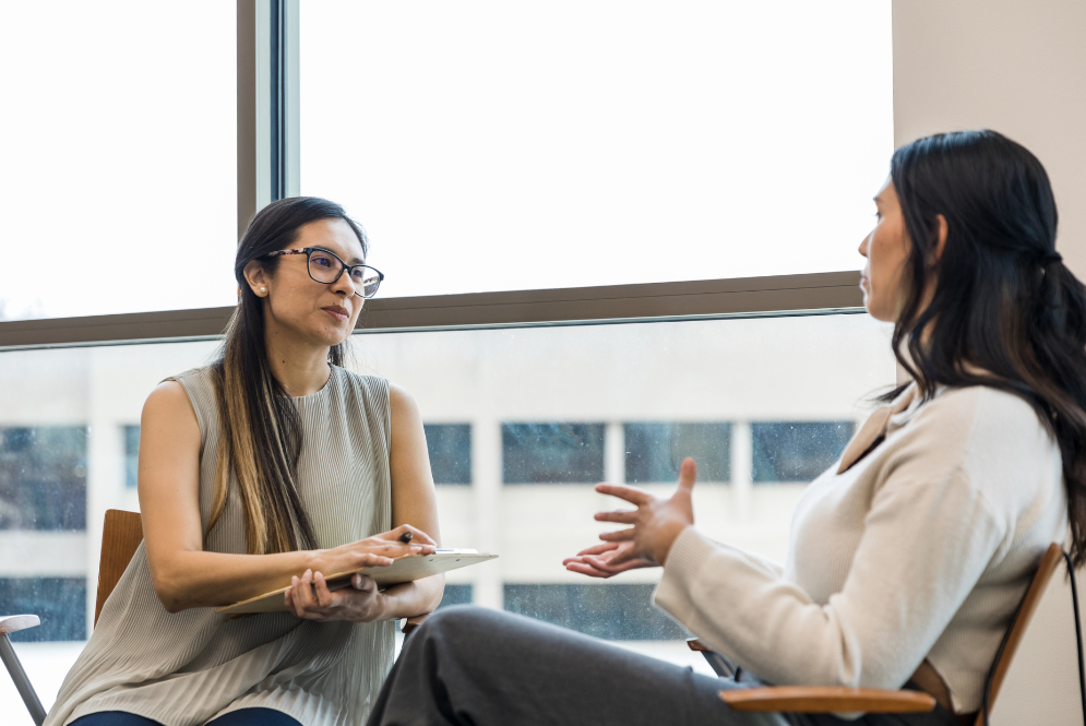 Two women are talking while one of them is holding a pen and a notebook - expand therapy practice