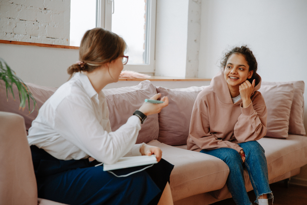 Two women sitting on a sofa, talking – Cash Pay Therapy.